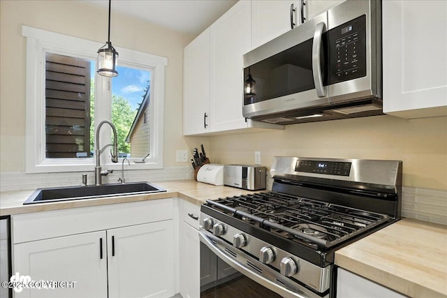 6622 Lakeway Dr, Anchorage, AK 99502 - kitchen featuring appliances with stainless steel finishes, white cabinetry, hanging light fixtures, wooden counters, and backsplash
