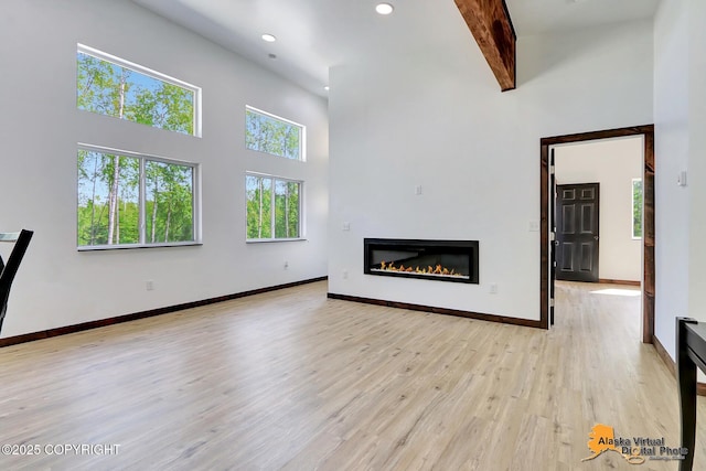 3528 S Mills Ct, Big Lake, AK 99623 - unfurnished living room with a high ceiling, a glass covered fireplace, recessed lighting, light wood-type flooring, and beam ceiling