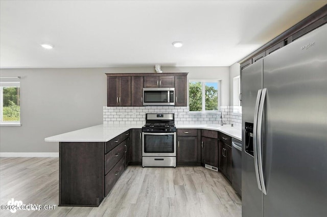 2740 S Rue De La Paix Loop, Wasilla, AK 99623 - kitchen featuring appliances with stainless steel finishes, a peninsula, light wood finished floors, dark brown cabinets, and tasteful backsplash