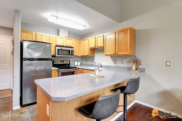 12231 Johns Rd # 2, Anchorage, AK 99515 - kitchen featuring appliances with stainless steel finishes, a peninsula, light brown cabinets, light countertops, and a breakfast bar