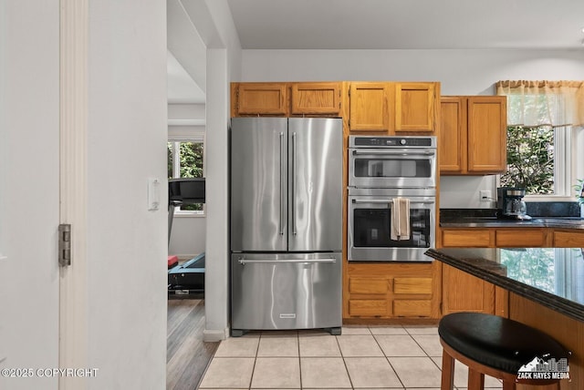 250 Botanical Cir, Anchorage, AK 99515 - kitchen with stainless steel appliances, brown cabinetry, dark stone countertops, and light tile patterned floors