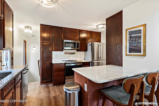 6922 Cutty Sark St, Anchorage, AK 99502 - kitchen with appliances with stainless steel finishes, light wood-style floors, a breakfast bar area, light stone countertops, and a peninsula