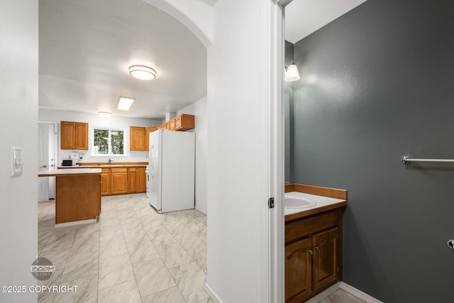5622 E 4th Ave Unit 12, Anchorage, AK 99504 - kitchen featuring white refrigerator with ice dispenser, light marble finish floors, brown cabinetry, arched walkways, and light countertops