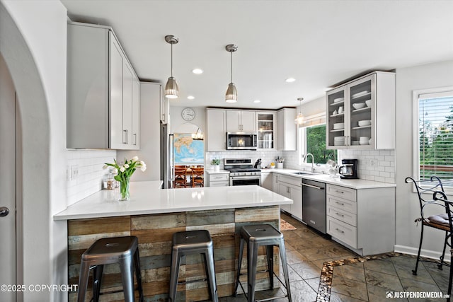 15250 Evergreen Ridge St, Anchorage, AK 99516 - kitchen with stainless steel appliances, a peninsula, backsplash, a breakfast bar, and glass insert cabinets