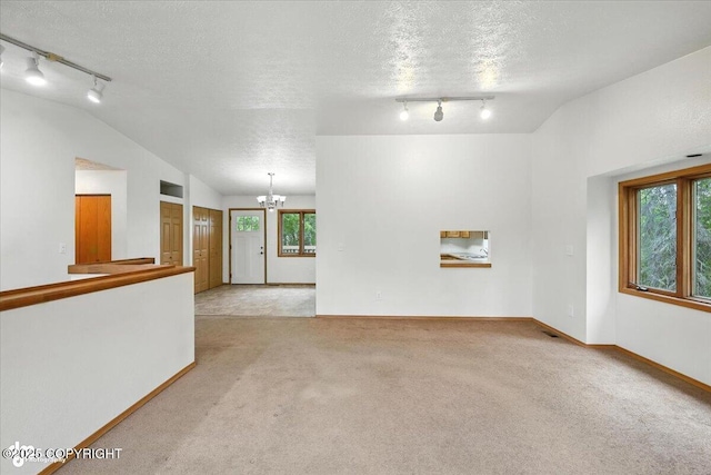 840 N Voss Cir, Wasilla, AK 99623 - unfurnished living room featuring rail lighting, lofted ceiling, a chandelier, plenty of natural light, and carpet flooring