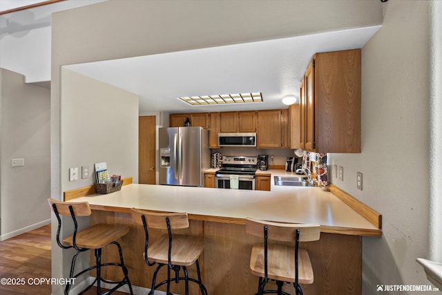 5170 Merle Cir, Anchorage, AK 99507 - kitchen with appliances with stainless steel finishes, light countertops, light wood-style flooring, brown cabinets, and a peninsula