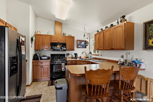 13693 E Guernsey Ln, Palmer, AK 99645 - kitchen featuring black appliances, a peninsula, vaulted ceiling, a breakfast bar area, and brown cabinets