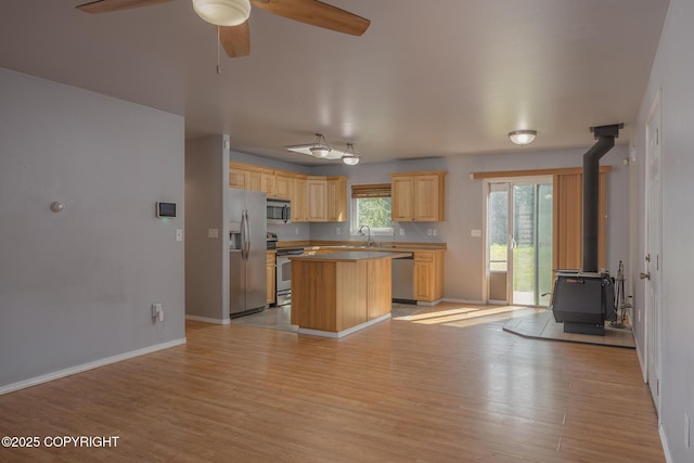 1250 Toolik Dr, North Pole, AK 99705 - kitchen with stainless steel appliances, a wood stove, light brown cabinets, a kitchen island, and light wood-style flooring