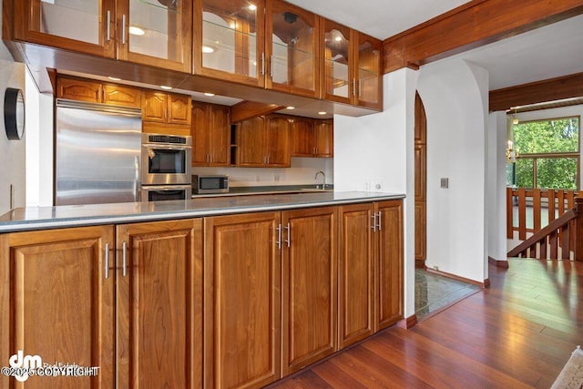 2107 Sorbus Way, Anchorage, AK 99508 - kitchen with appliances with stainless steel finishes, dark wood finished floors, brown cabinetry, glass insert cabinets, and arched walkways