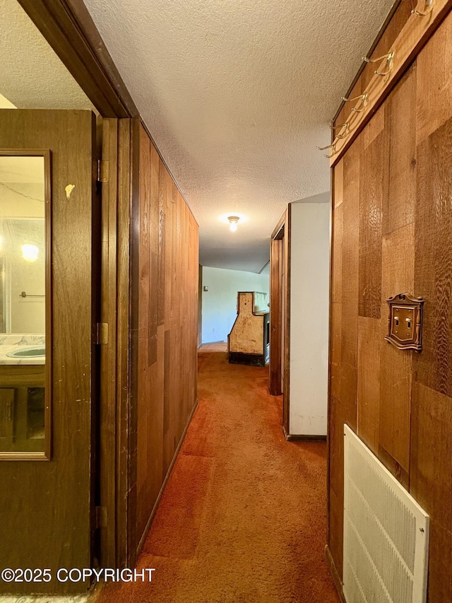 8204 E 17th Ave, Anchorage, AK 99504 - hall featuring a textured ceiling, carpet flooring, and wood walls