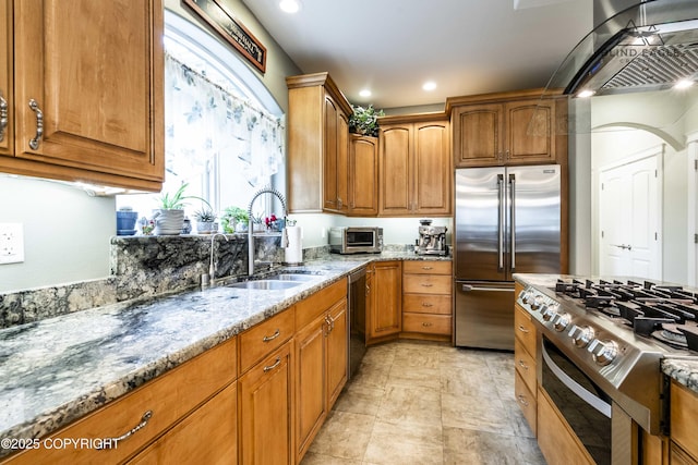 17237 E Smith Rd, Palmer, AK 99645 - kitchen featuring appliances with stainless steel finishes, light stone countertops, wall chimney exhaust hood, brown cabinetry, and recessed lighting