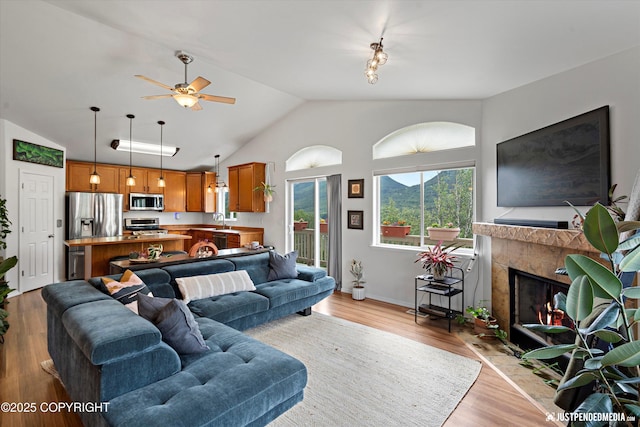 9166 Eagle River Ln, Eagle River, AK 99577 - living room featuring vaulted ceiling, ceiling fan, light wood-style flooring, and a tiled fireplace