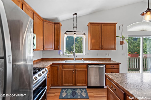 9166 Eagle River Ln, Eagle River, AK 99577 - kitchen with stainless steel appliances, vaulted ceiling, brown cabinetry, and decorative light fixtures