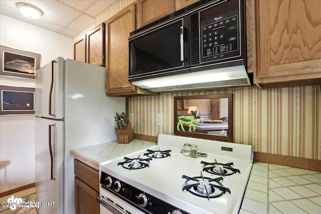 311 Alpine Meadows Ave, Girdwood, AK 99587 - kitchen with gas range gas stove, black microwave, tile countertops, brown cabinetry, and tile patterned floors