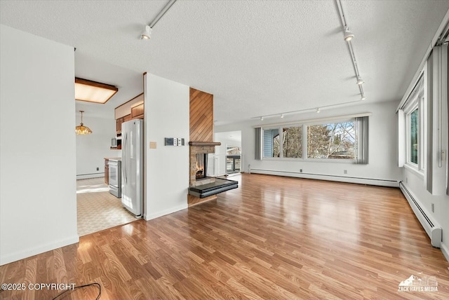 1521 Cache Dr, Anchorage, AK 99507 - unfurnished living room with rail lighting, a baseboard radiator, light wood-style floors, a multi sided fireplace, and a textured ceiling