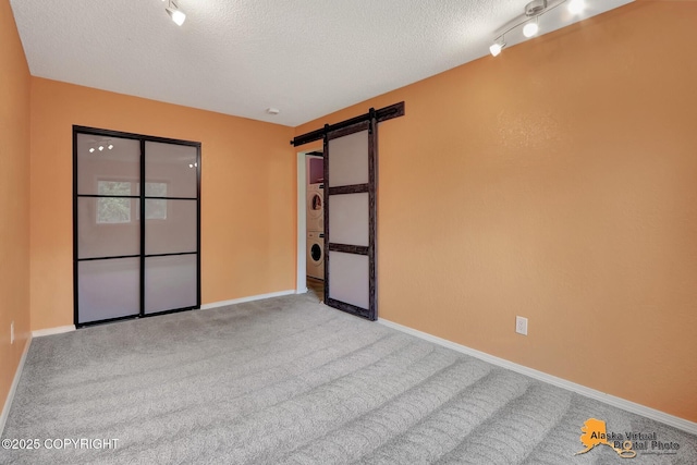 3265 Montclair Ct # 17E, Anchorage, AK 99503 - empty room with stacked washing machine and dryer, a textured ceiling, a barn door, and carpet floors
