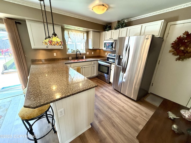 3920 Red Talon Dr, Anchorage, AK 99507 - kitchen with appliances with stainless steel finishes, a peninsula, light wood-style floors, white cabinets, and pendant lighting