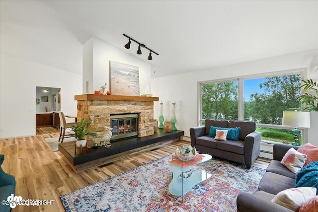 3291 N Edgewater Dr, Wasilla, AK 99623 - living room with track lighting, wood finished floors, a baseboard heating unit, a stone fireplace, and vaulted ceiling