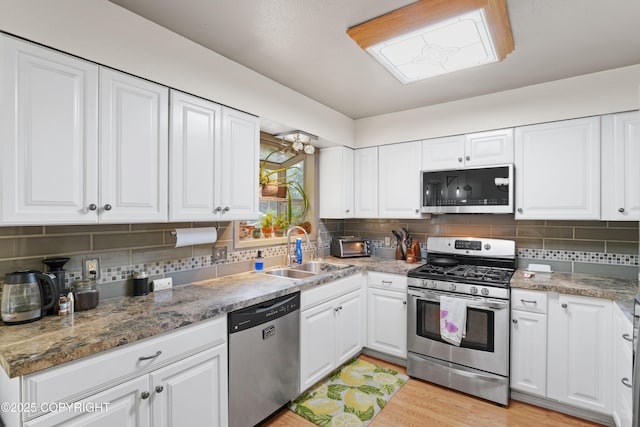 10711 Colville St, Eagle River, AK 99577 - kitchen featuring appliances with stainless steel finishes, white cabinets, tasteful backsplash, and light wood-type flooring