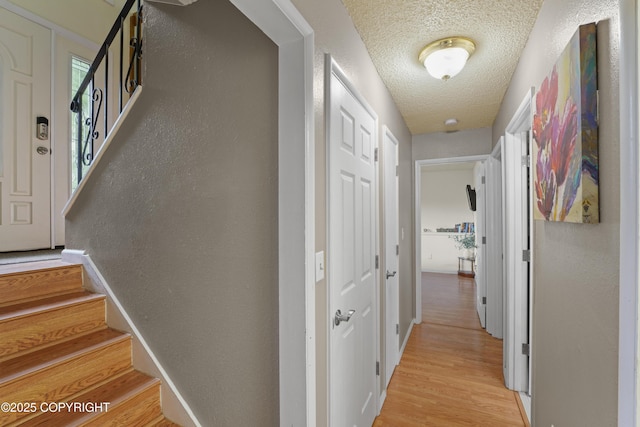10711 Colville St, Eagle River, AK 99577 - hallway with a textured ceiling, stairway, a textured wall, and light wood-style flooring