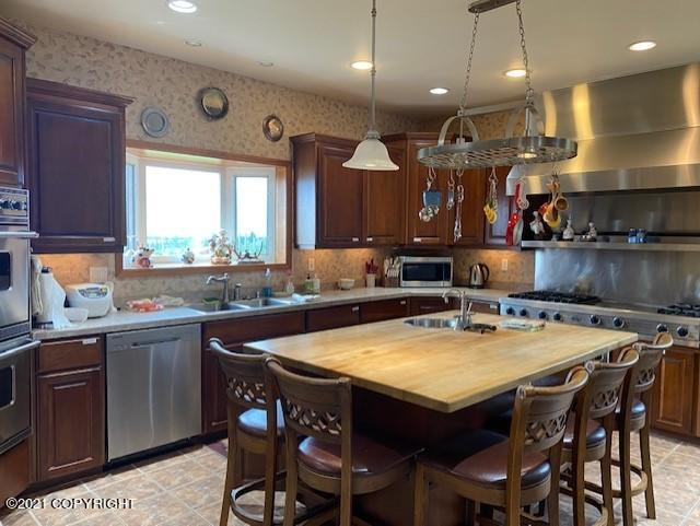60871 Bear Creek Dr, Homer, AK 99603 - kitchen with appliances with stainless steel finishes, butcher block counters, wall chimney exhaust hood, a breakfast bar area, and an island with sink
