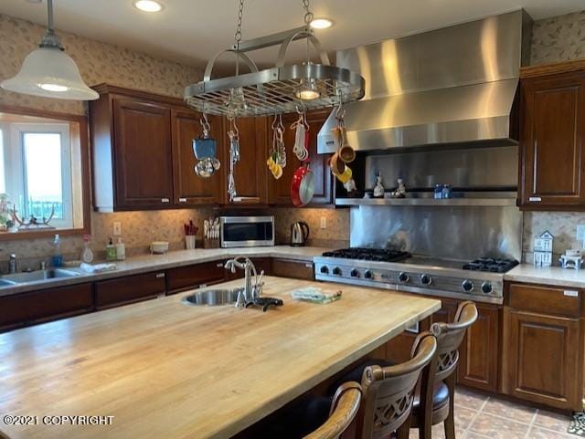 60871 Bear Creek Dr, Homer, AK 99603 - kitchen featuring butcher block countertops, appliances with stainless steel finishes, wall chimney range hood, a kitchen bar, and recessed lighting