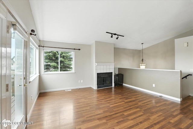 10300 Ridge Park Dr, Anchorage, AK 99507 - unfurnished living room featuring wood finished floors, a tiled fireplace, track lighting, and vaulted ceiling