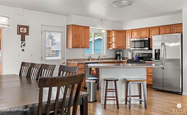8430 Greenhill Way, Anchorage, AK 99502 - kitchen with appliances with stainless steel finishes, brown cabinetry, a breakfast bar, light wood-type flooring, and a textured ceiling