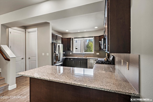 11459 Moonrise Ridge Pl # 7, Anchorage, AK 99516 - kitchen with appliances with stainless steel finishes, dark brown cabinetry, light wood-style flooring, tasteful backsplash, and a peninsula