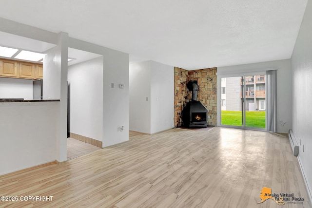 4650 Reka Dr # F6, Anchorage, AK 99508 - unfurnished living room with light wood-style flooring, baseboard heating, and a wood stove
