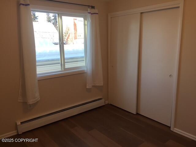 420 E 14th Ave, Anchorage, AK 99501 - unfurnished bedroom featuring a baseboard heating unit, a closet, multiple windows, and wood finished floors