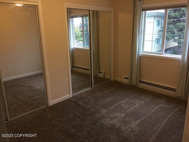 420 E 14th Ave, Anchorage, AK 99501 - unfurnished bedroom featuring dark colored carpet, multiple windows, two closets, and baseboard heating