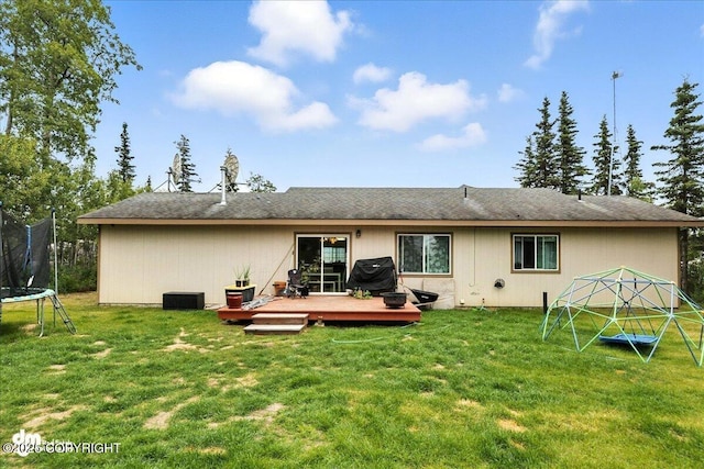 34443 Matanuska St, Soldotna, AK 99669 - back of property featuring a trampoline, roof with shingles, a wooden deck, and a lawn