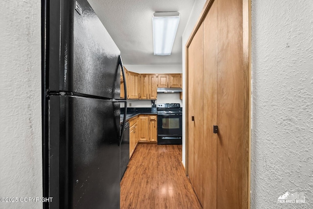 8641 Blackberry St # 6B, Anchorage, AK 99502 - kitchen with black appliances, a textured wall, under cabinet range hood, wood finished floors, and dark countertops