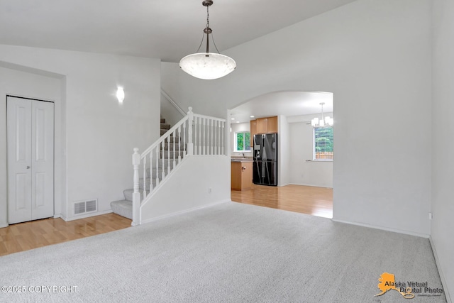 2321 Lusardi Point Cir, Anchorage, AK 99515 - unfurnished living room with light colored carpet, arched walkways, stairs, a chandelier, and light wood-style flooring