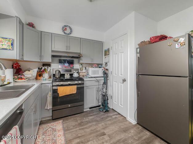 282 Marydale Ct, Soldotna, AK 99669 - kitchen featuring appliances with stainless steel finishes, gray cabinetry, under cabinet range hood, light countertops, and light wood-style flooring