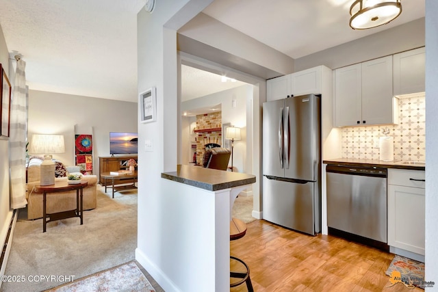 4840 Bryn Mawr Ct Unit 3, Anchorage, AK 99508 - kitchen with stainless steel appliances, dark countertops, white cabinetry, a brick fireplace, and decorative backsplash