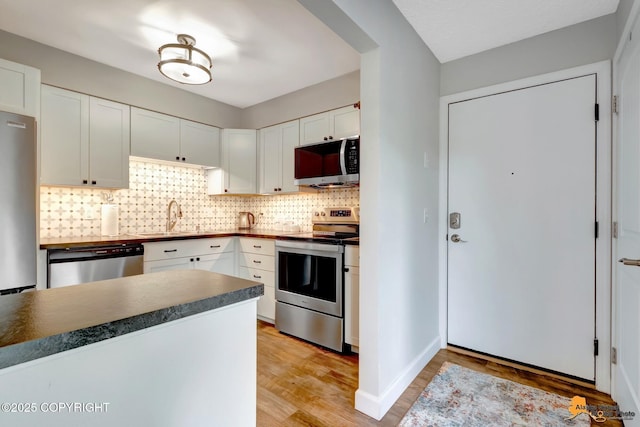 4840 Bryn Mawr Ct Unit 3, Anchorage, AK 99508 - kitchen with stainless steel appliances, dark countertops, backsplash, light wood-type flooring, and white cabinetry