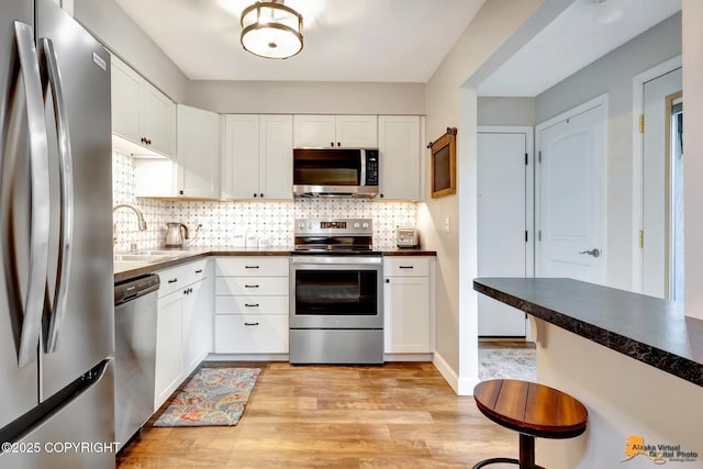 4840 Bryn Mawr Ct Unit 3, Anchorage, AK 99508 - kitchen featuring stainless steel appliances, light wood-style flooring, white cabinets, backsplash, and dark countertops
