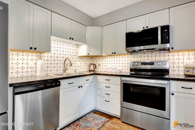 4840 Bryn Mawr Ct Unit 3, Anchorage, AK 99508 - kitchen featuring appliances with stainless steel finishes, dark countertops, backsplash, white cabinets, and light wood-type flooring