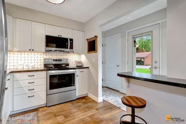 4840 Bryn Mawr Ct Unit 3, Anchorage, AK 99508 - kitchen featuring stainless steel appliances, dark countertops, white cabinetry, tasteful backsplash, and light wood-style flooring