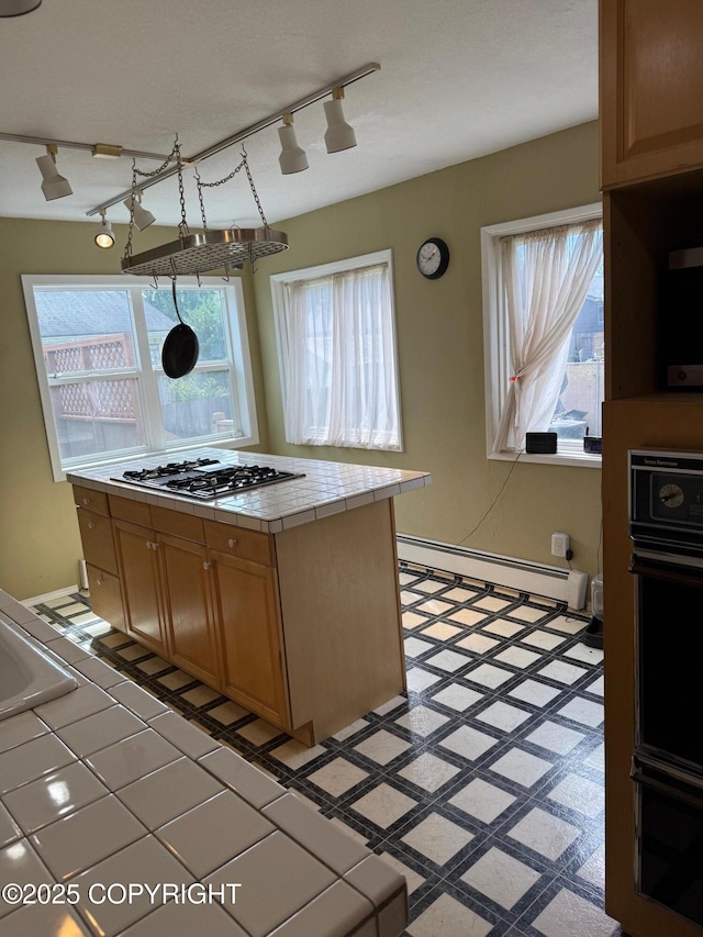 2090 Dimond Dr, Anchorage, AK 99507 - kitchen with tile counters, baseboard heating, stainless steel gas cooktop, track lighting, and plenty of natural light