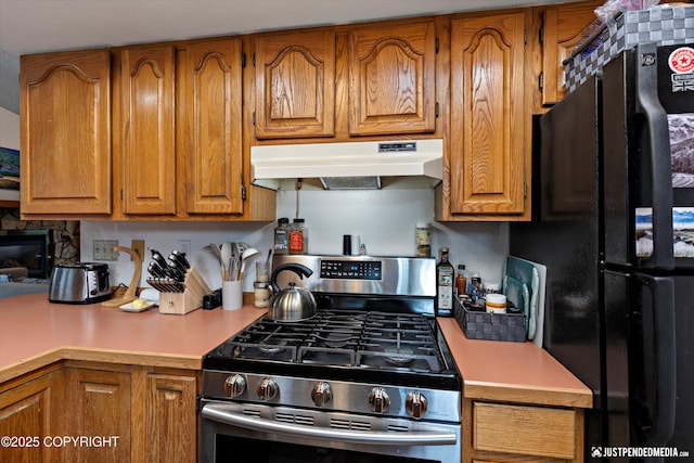 260 N Gloria St, Palmer, AK 99645 - kitchen with freestanding refrigerator, gas stove, under cabinet range hood, brown cabinetry, and light countertops