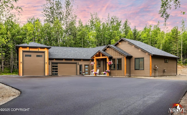 365 W Crestwood Ave, Wasilla, AK 99654 - view of front of property featuring an attached garage, asphalt driveway, board and batten siding, roof with shingles, and view of wooded area