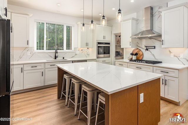 365 W Crestwood Ave, Wasilla, AK 99654 - kitchen with wall chimney exhaust hood, appliances with stainless steel finishes, a kitchen island, light wood finished floors, and white cabinetry
