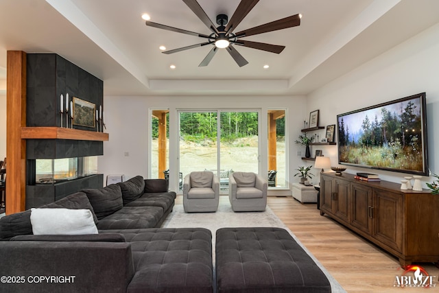 365 W Crestwood Ave, Wasilla, AK 99654 - living room featuring a tray ceiling, light wood-type flooring, a ceiling fan, a multi sided fireplace, and recessed lighting