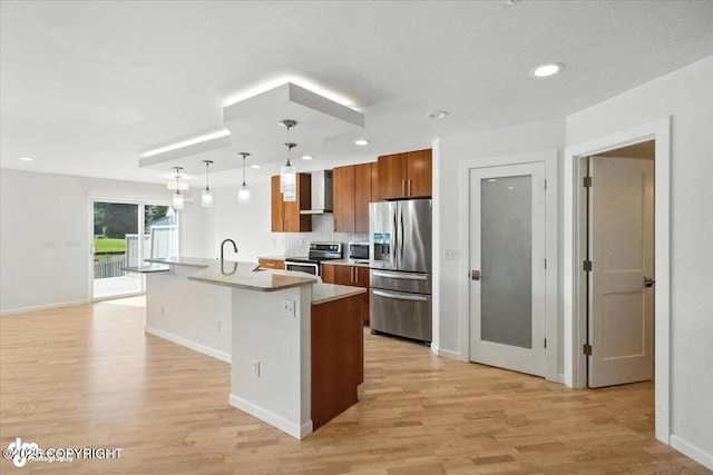 2350 Canary Ct, Anchorage, AK 99515 - kitchen featuring appliances with stainless steel finishes, wall chimney exhaust hood, brown cabinets, light wood finished floors, and a kitchen island with sink