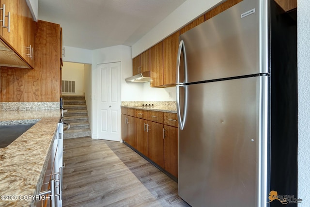 2350 Canary Ct, Anchorage, AK 99515 - kitchen with freestanding refrigerator, brown cabinetry, light wood-type flooring, under cabinet range hood, and light stone counters