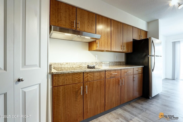 2350 Canary Ct, Anchorage, AK 99515 - kitchen with under cabinet range hood, freestanding refrigerator, black electric cooktop, light wood-style flooring, and brown cabinets
