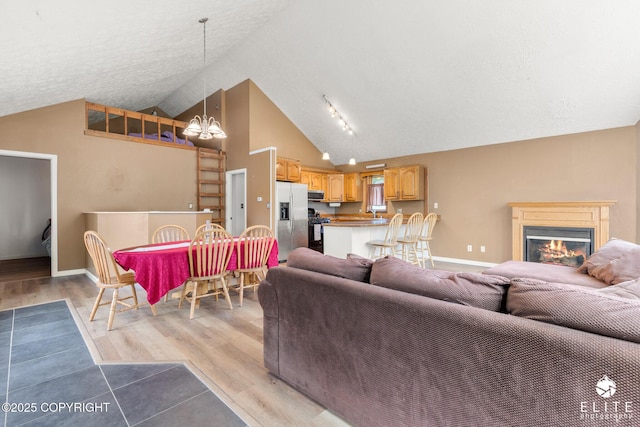 3021 N Arctic Fox Dr, Wasilla, AK 99654 - living room with a chandelier, light wood-style flooring, a glass covered fireplace, a textured ceiling, and high vaulted ceiling
